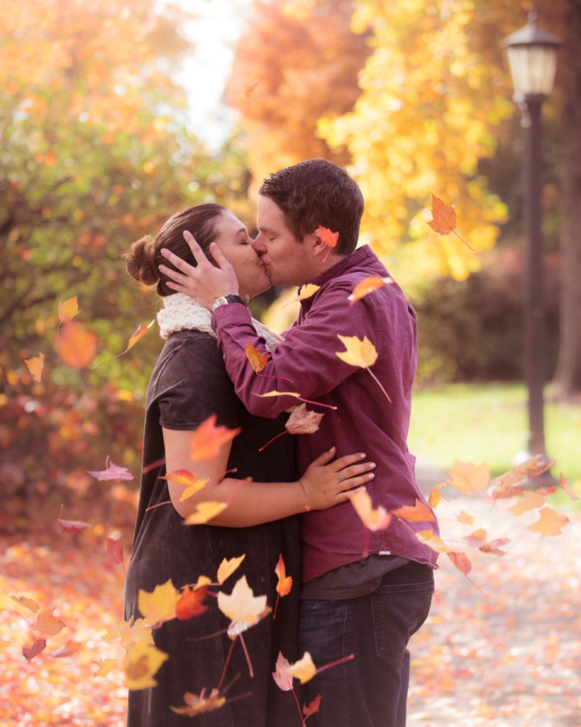 A fall portrait of leaves falling as a couple kisses at Oregon State University, taken by Corvallis Portraits.